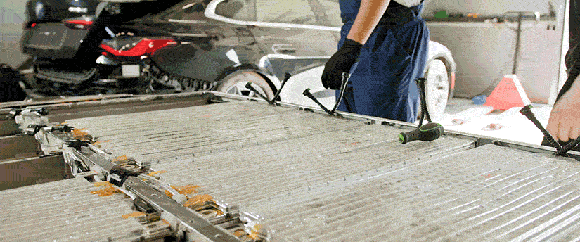 A man is focused on repairing a car battery, tools in hand, in a well-lit garage environment.

