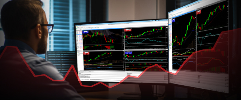 Un homme concentré analyse des graphiques boursiers sur un écran d’ordinateur, entouré de documents financiers.