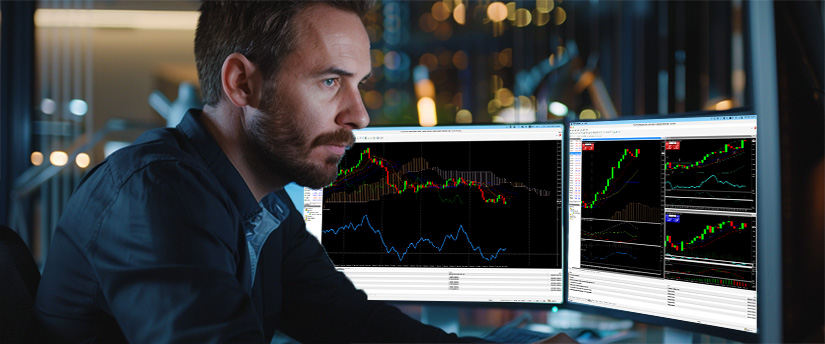 A man at a desk with two monitors displaying different forex trading platforms for beginners.