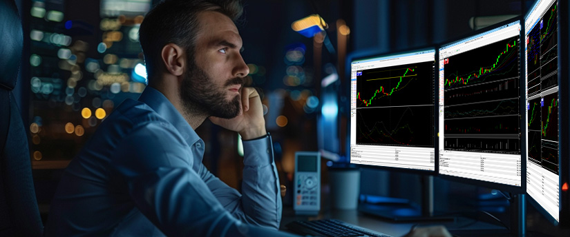 A man intently watches multiple computer monitors displaying financial charts at night, reflecting forex fundamental analysis in a focused trading environment.